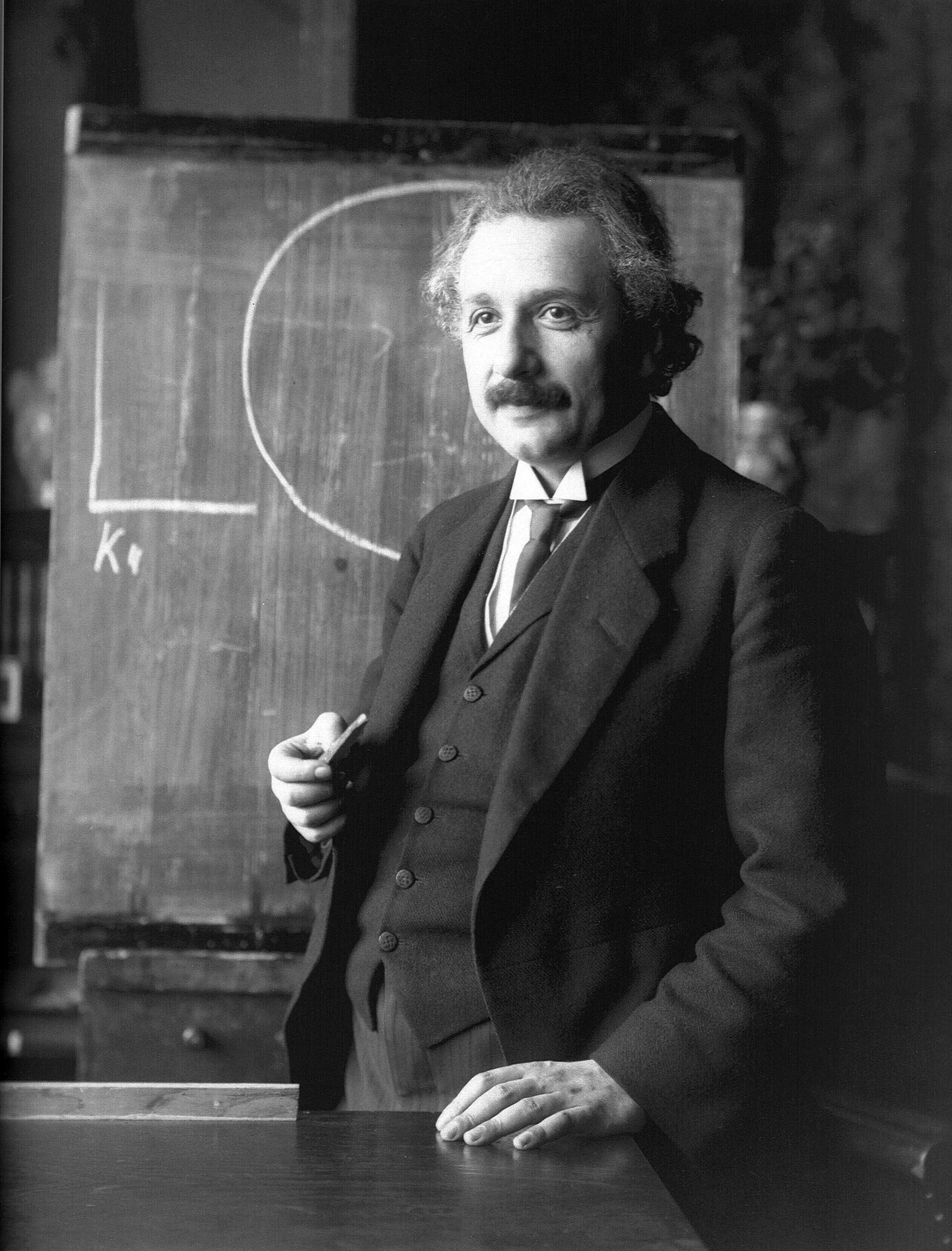 Albert Einstein standing beside a blackboard with chalk equations