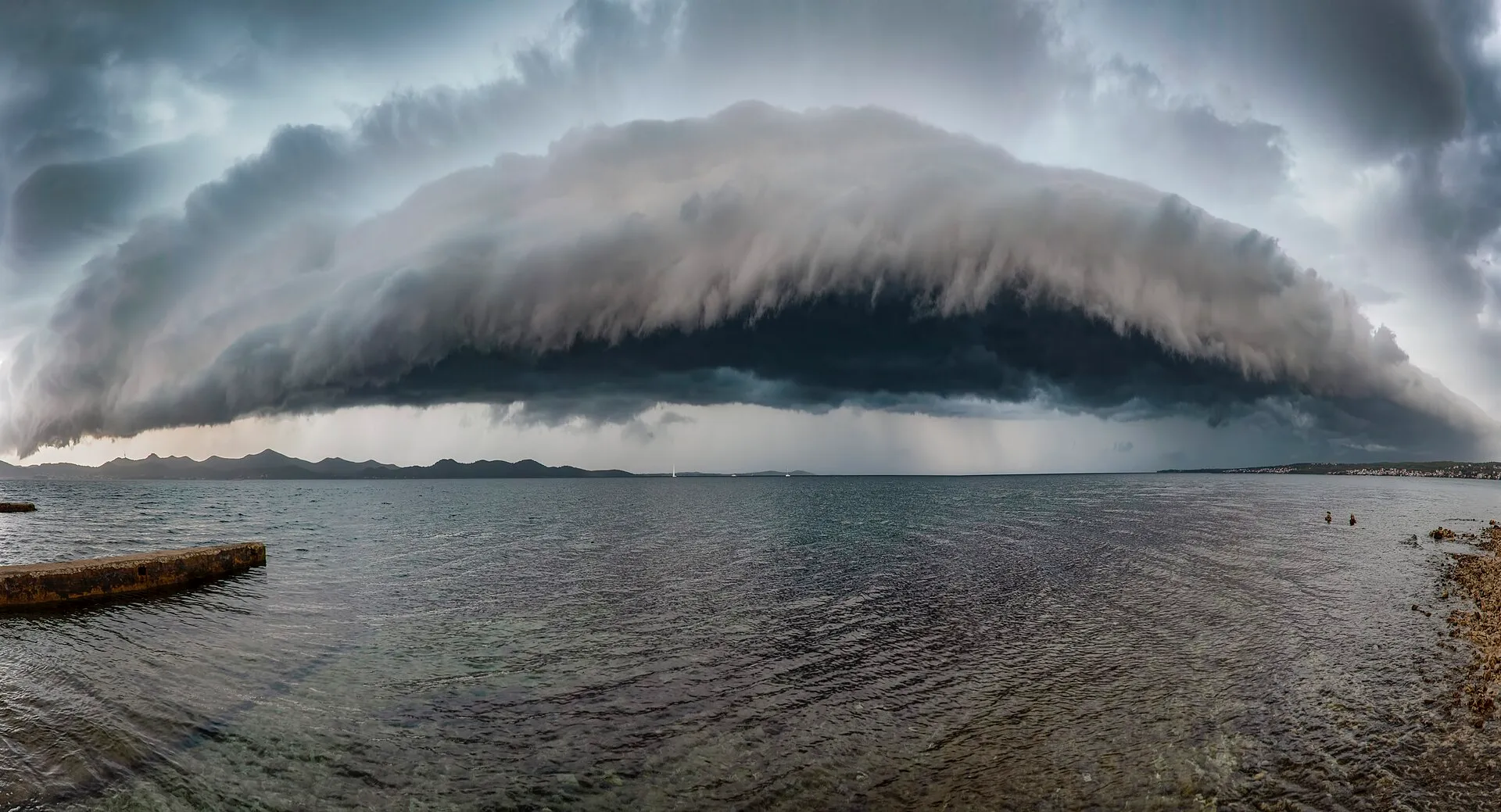 Dark shelf cloud rolling over a lake ahead of a storm