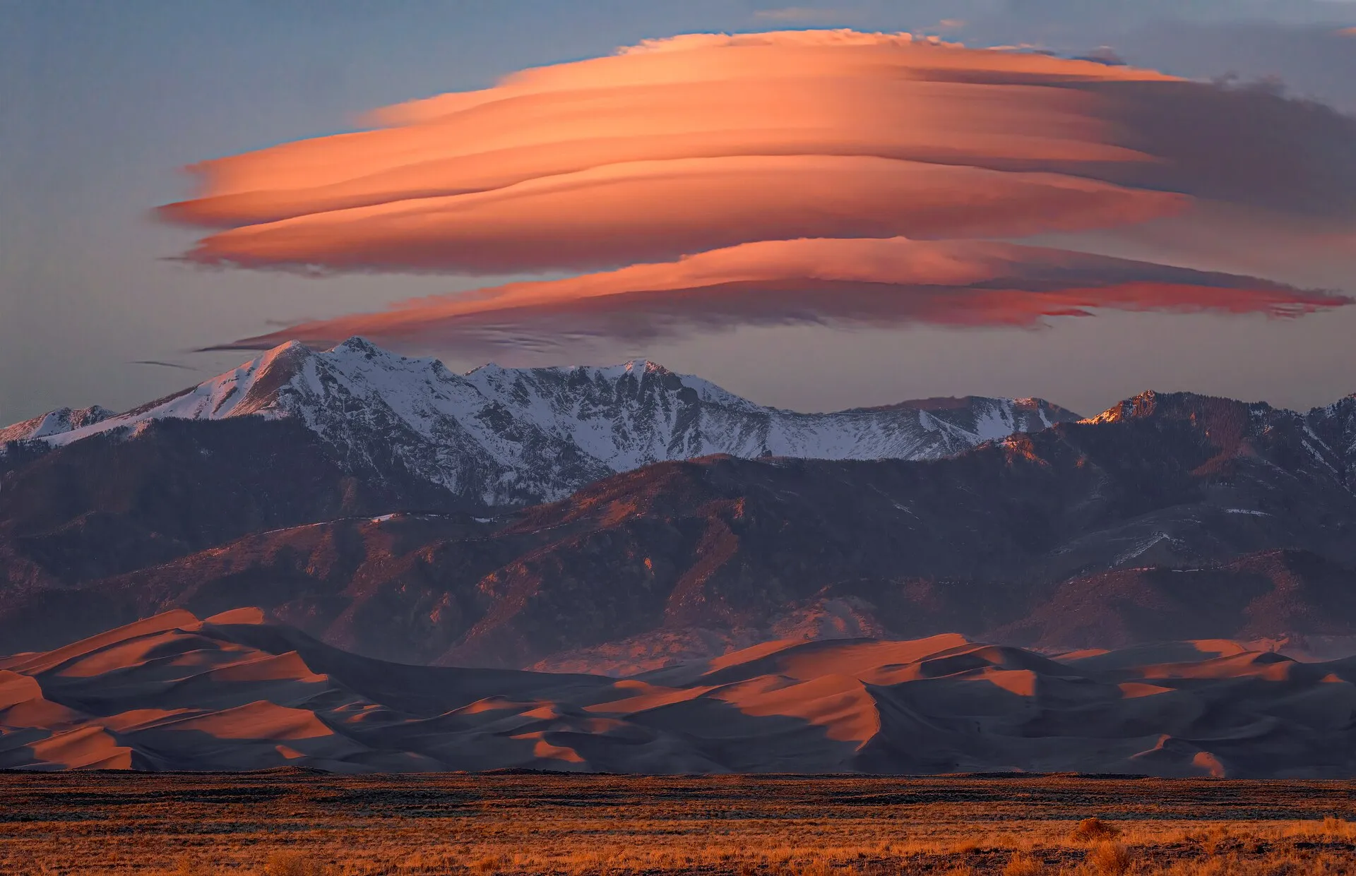 Orange lenticular cloud hovering over mountains at sunset