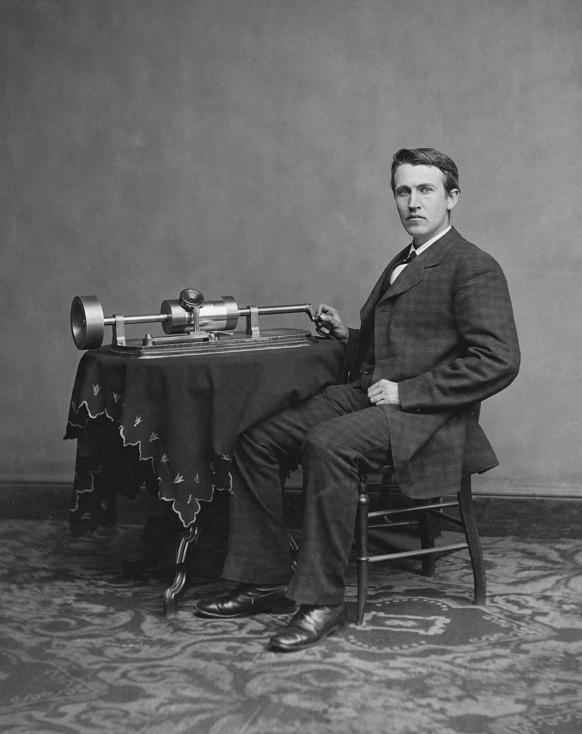Young Thomas Edison seated beside his early phonograph