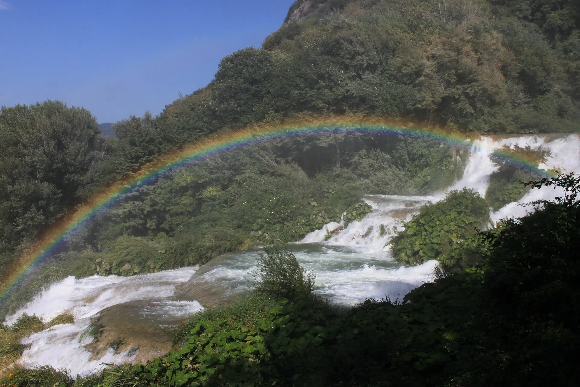 Rainbow forming in the spray above a broad waterfall