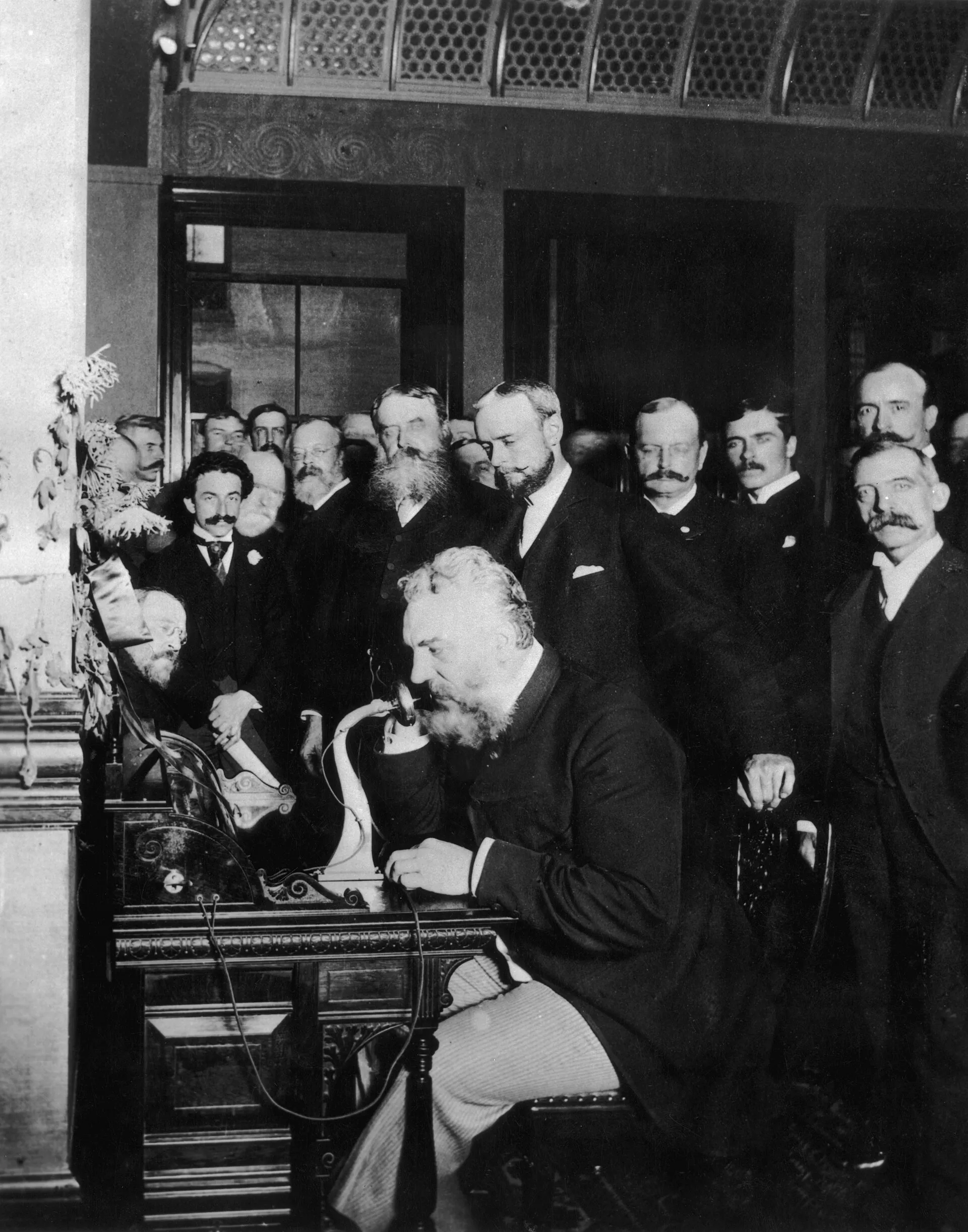 Alexander Graham Bell speaking into an early telephone before onlookers