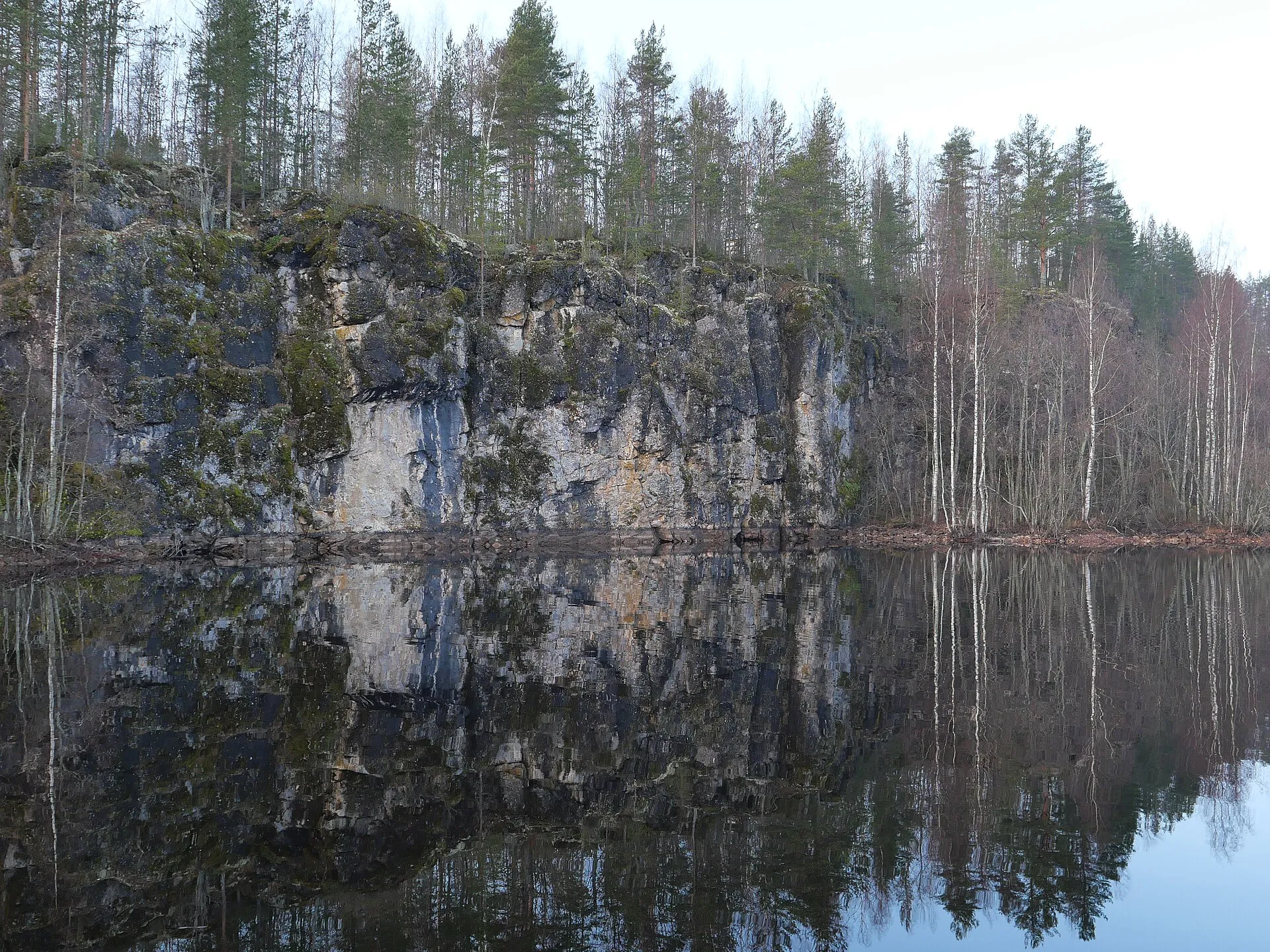 Sheer quarried rock face reflected in a still forest lake