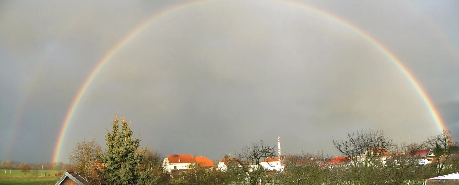 Double rainbow arcing over a village with both bows visible